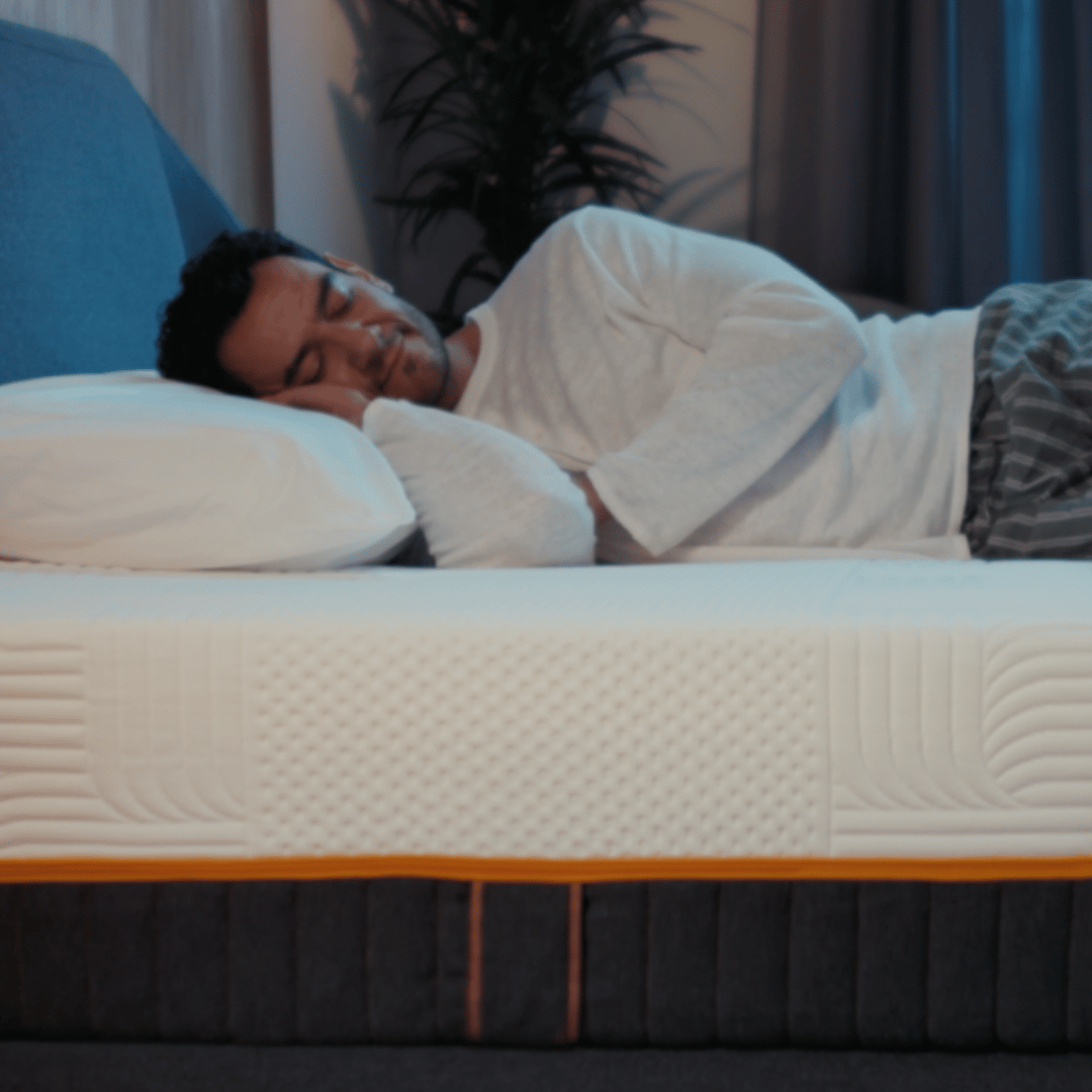 Een man die slaapt op een Emma Performance-boxspringbed met een gewatteerde matras en een met antraciet bekleed onderstel in een gezellige slaapkamer.