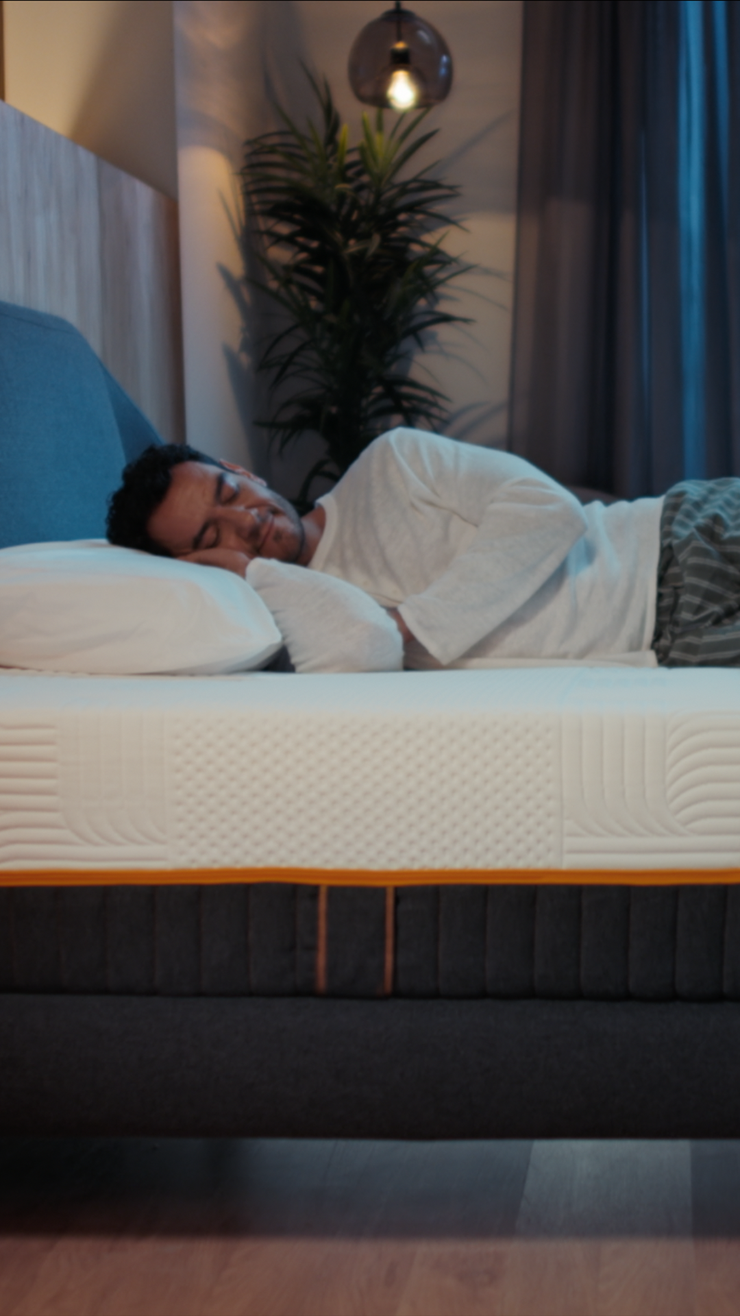 Een man die slaapt op een Emma Performance-boxspringbed met een gewatteerde matras en een met antraciet bekleed onderstel in een gezellige slaapkamer.