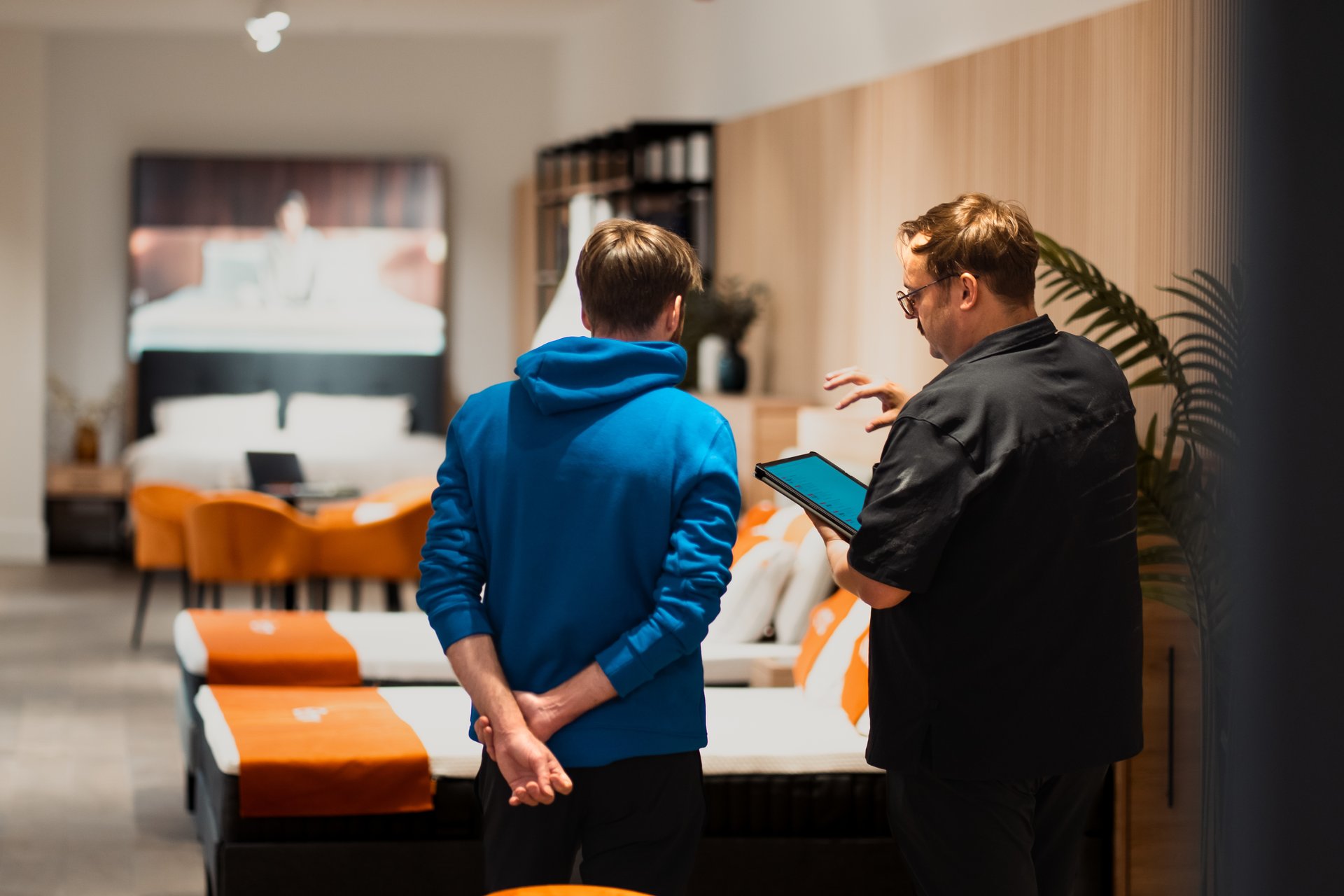Deux hommes discutent dans un magasin Emma, entourés de lits et de coussins orange.
