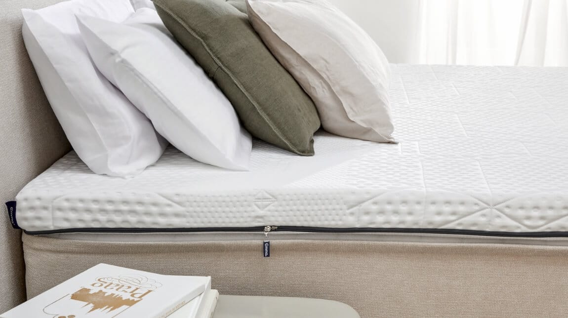 topper con quattro cuscini colorati e comodino con libro, illuminato da luce naturale.