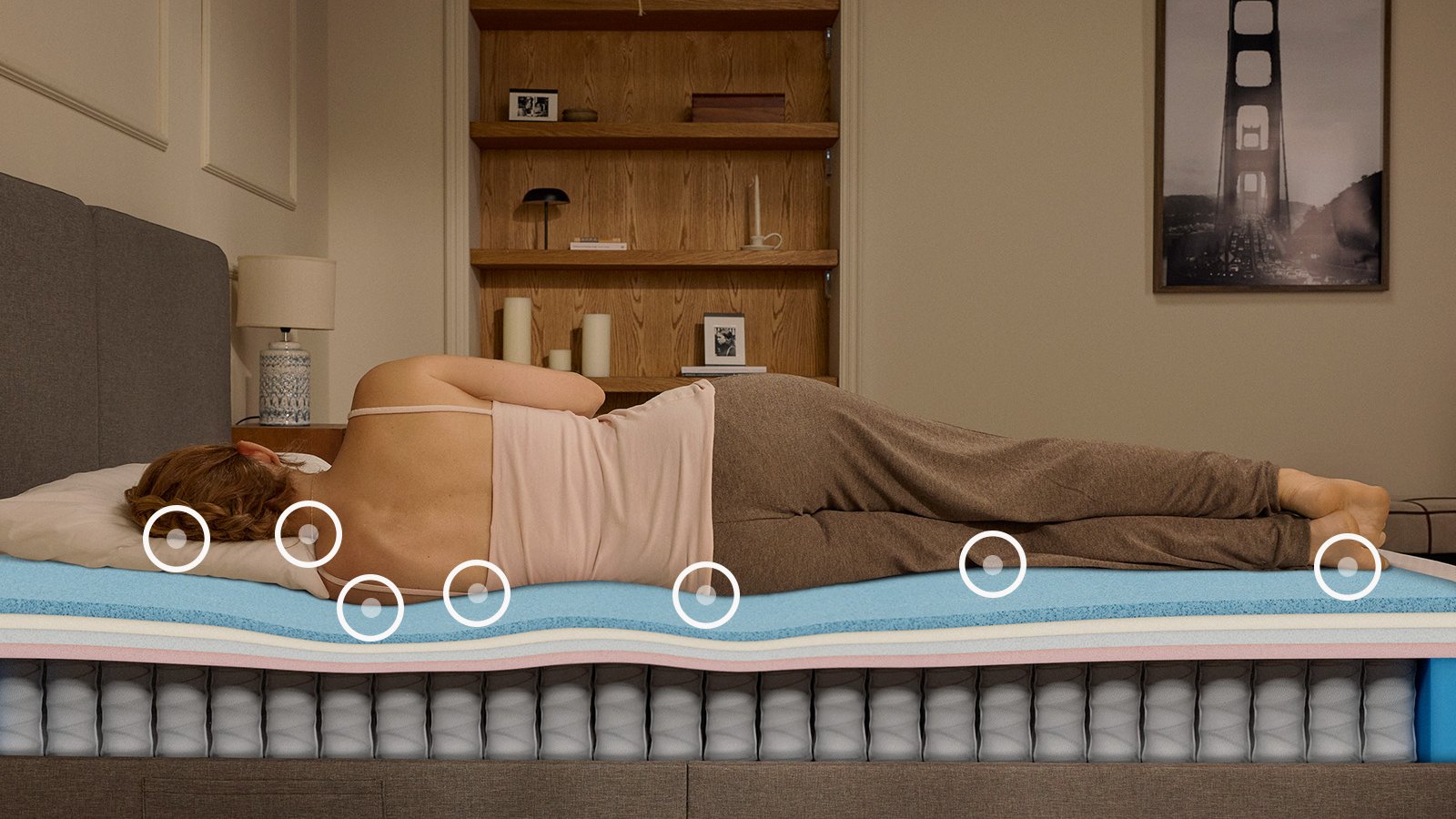 Woman sleeping on her side on an Emma Original Pro mattress, with foam and spring layers visible beneath her.