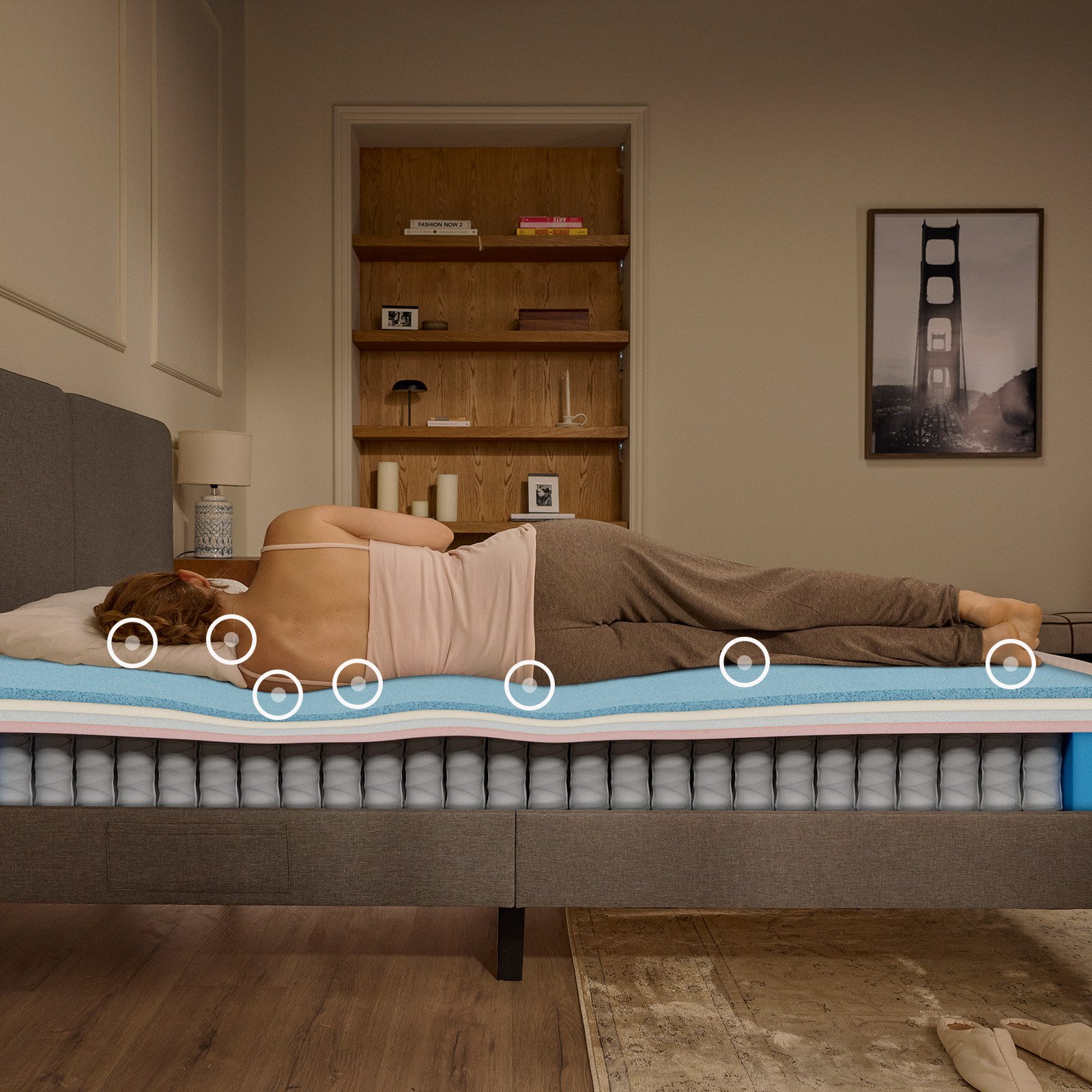 Woman sleeping on her side on an Emma mattress in a warmly lit bedroom, with a cutaway view of the mattress showing foam comfort layers and individually wrapped pocket springs adapting to her body's pressure points