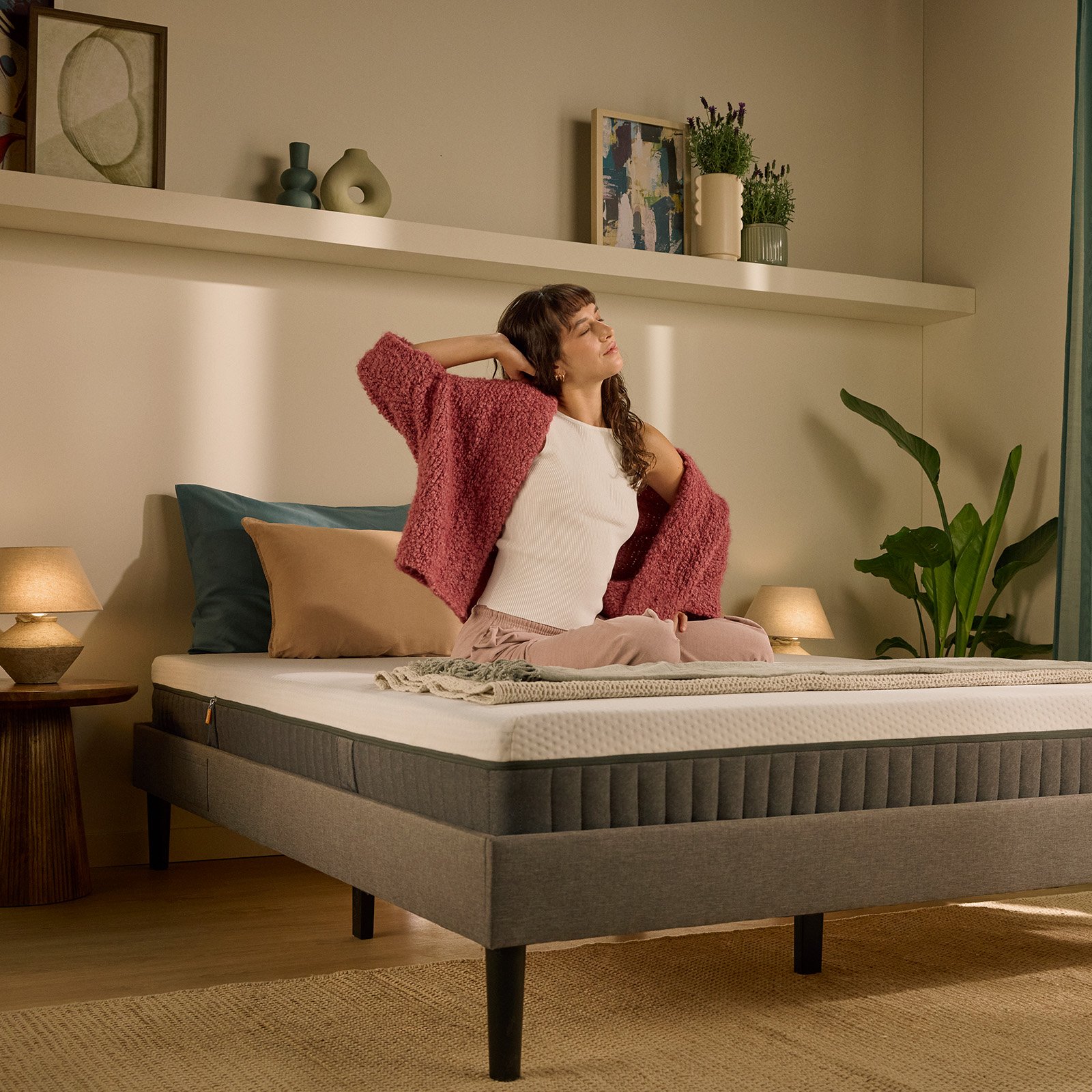 Person sitting up on a bed with a white mattress in the morning.
