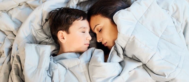 Femme et enfant dormant sur un lit avec une couette.