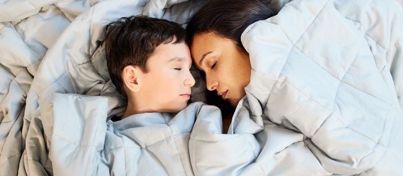 Femme et enfant dormant sur un lit avec une couette.