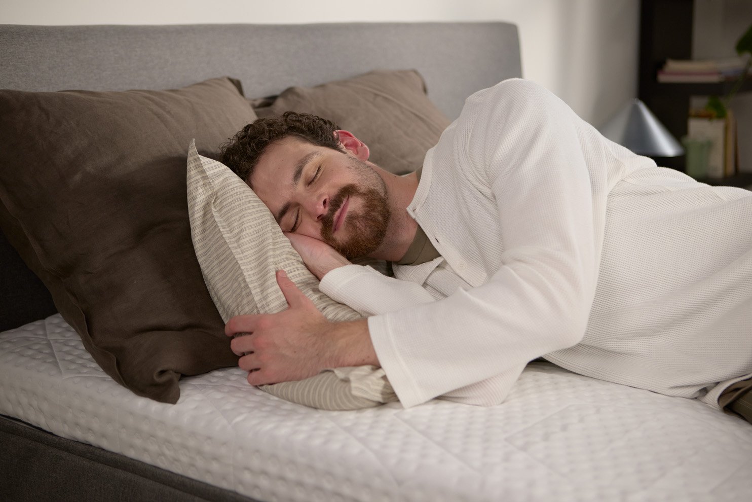Person comfortably sleeping on their side on a textured mattress topper, with supportive pillow and neutral bedding.