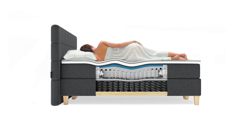 Frau liegt seitlich auf einem Boxspringbett mit sichtbarem Schichtaufbau der Matratze.