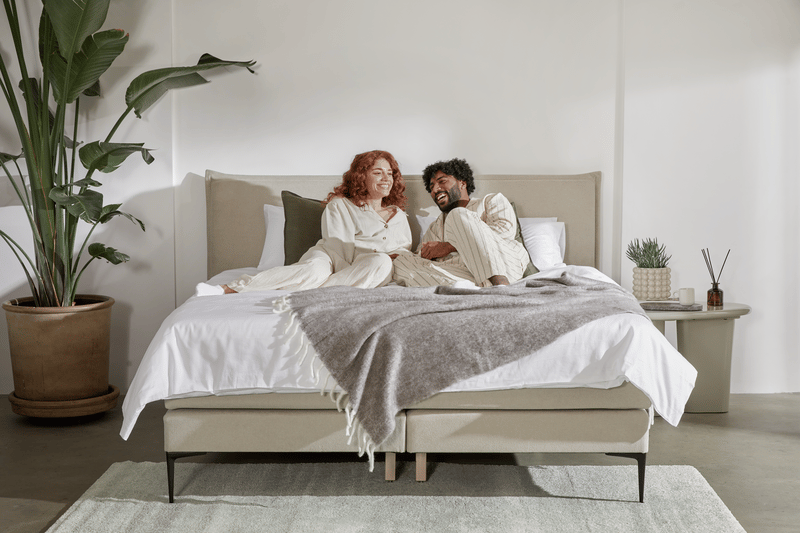 Paar in Pyjamas lacht zusammen auf einem Emma Boxspringbett.