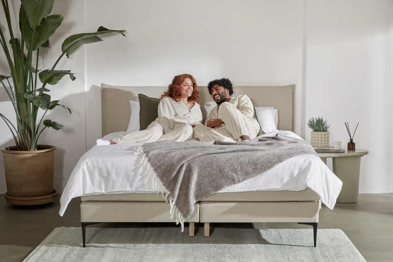 Paar in Pyjamas lacht zusammen auf einem Emma Boxspringbett.