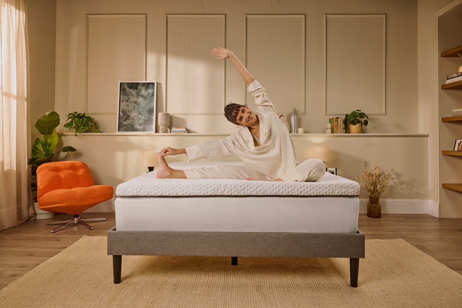 Persoon die stretchoefeningen doet op een matras in een warm ingerichte slaapkamer.