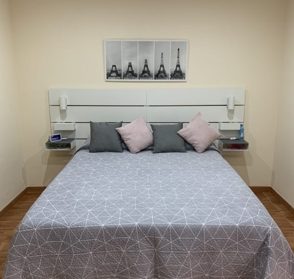 Cama con sabanas grises y 4 almohadas encima en una habitación bien decorada