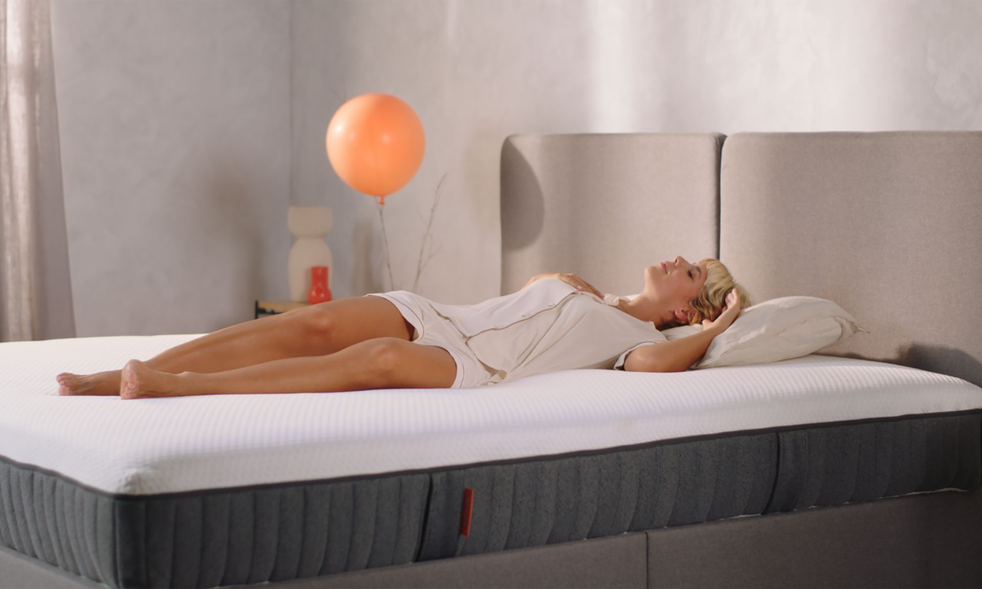 Persona su letto con testiera grigia e palloncino arancione sullo sfondo.