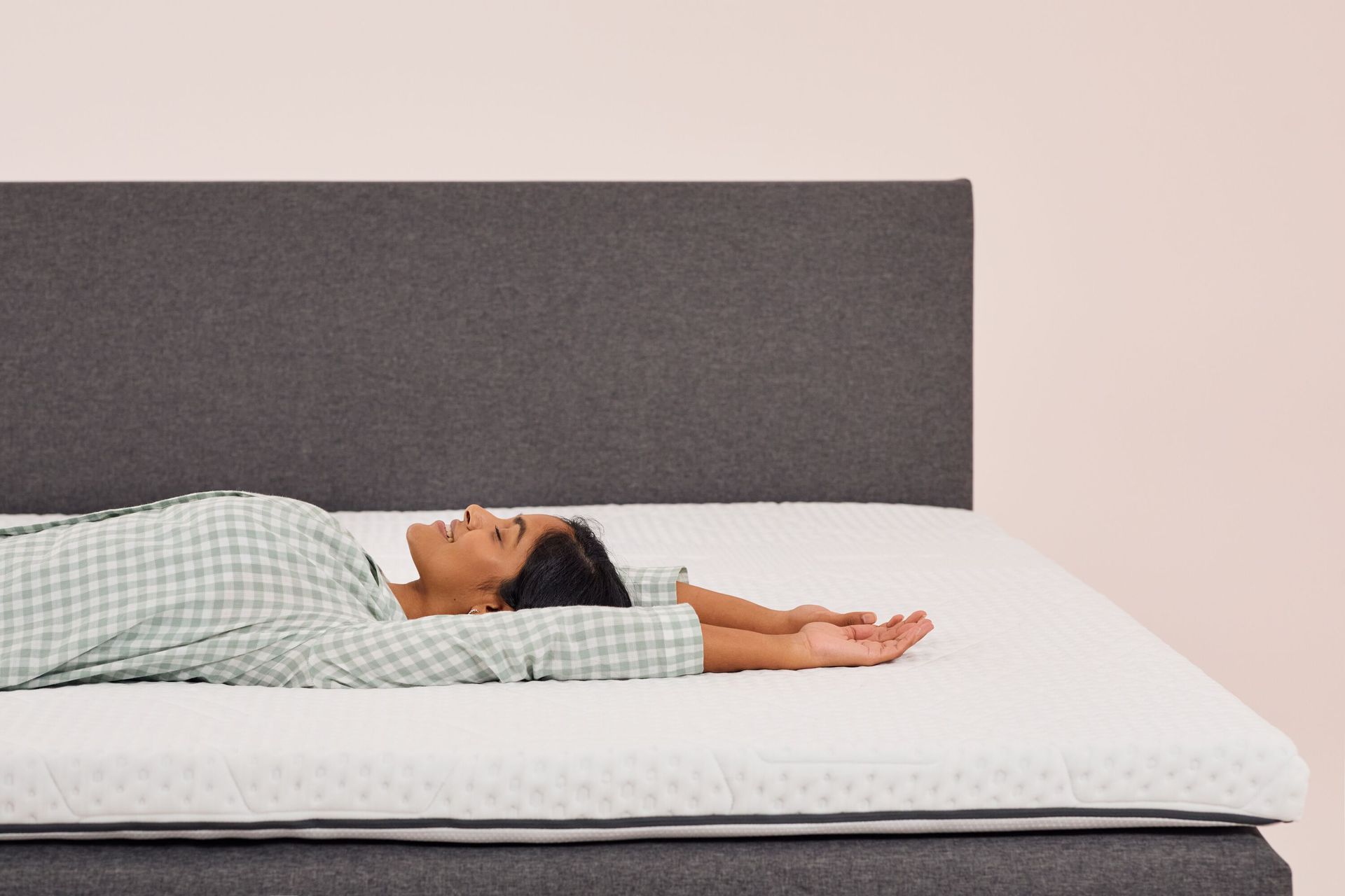 Frau liegt entspannt auf einem Emma Topper mit grauem Kopfteil im Hintergrund.