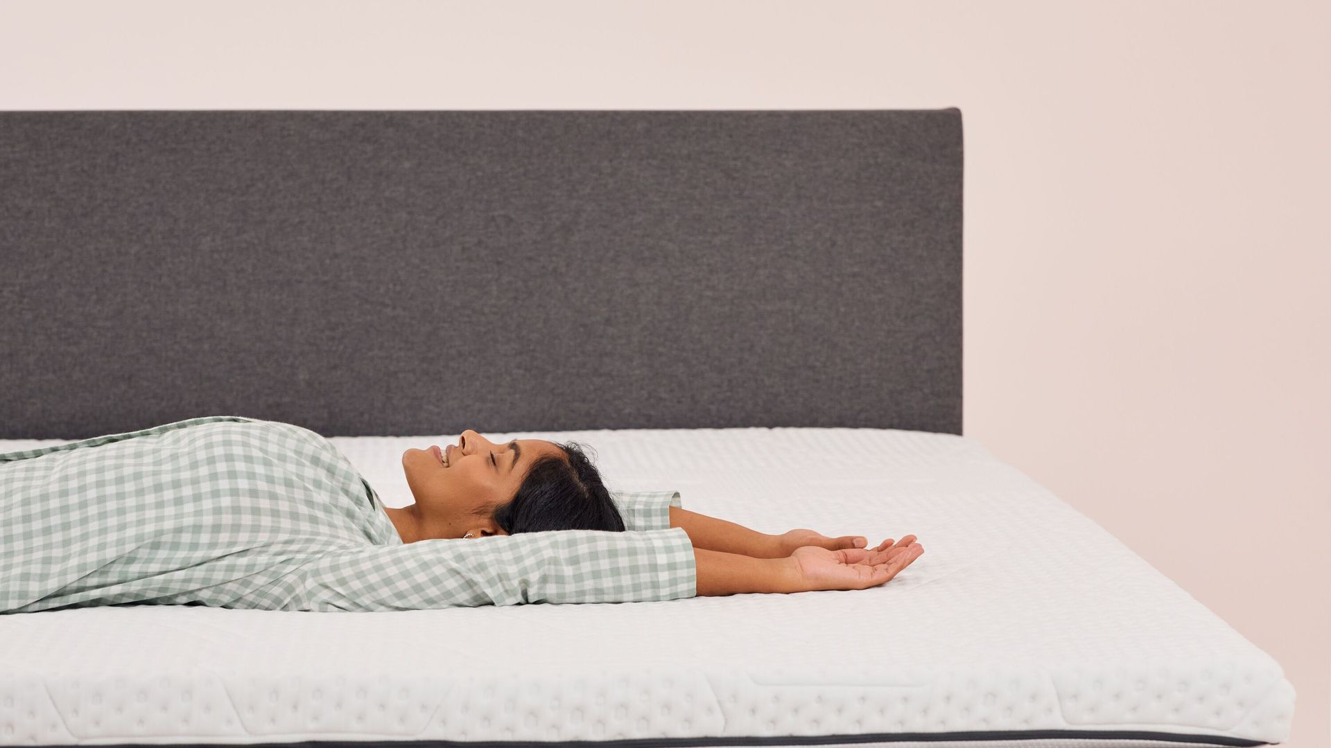 Frau liegt entspannt auf einem Emma Topper mit grauem Kopfteil im Hintergrund.