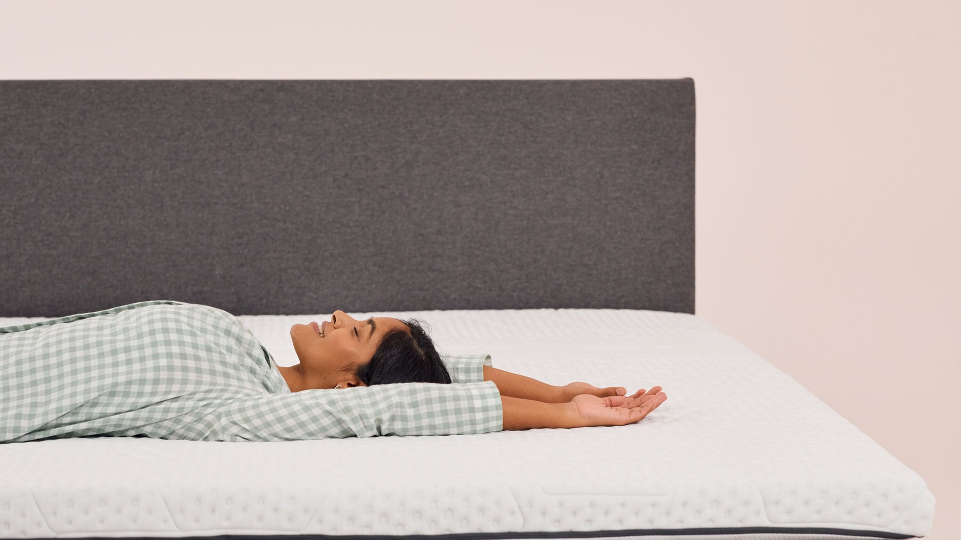 Frau liegt entspannt auf einem Emma Topper mit grauem Kopfteil im Hintergrund.