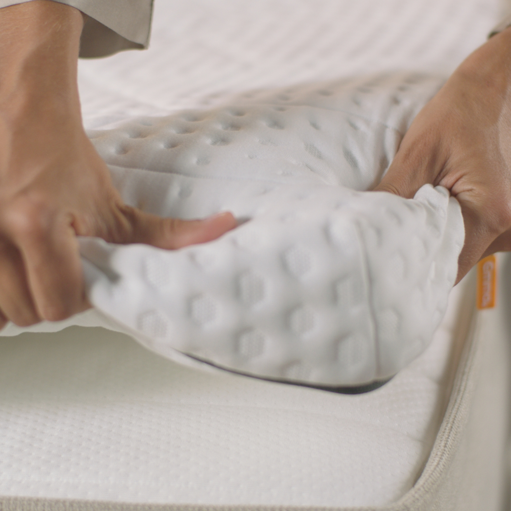 Deux mains ajustant un surmatelas blanc texturé sur un matelas.
