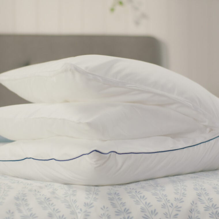 Original Cooling Comfort Kussen op bed om alle verwijderbare lagen te zien. Op de achtergrond staat een grijs gestoffeerd hoofdbord en een gele lamp op een nachtkastje. Deze afbeelding toont het luchtige en stijlvolle ontwerp van het Emma Wolkenkussen in een huiselijke setting.