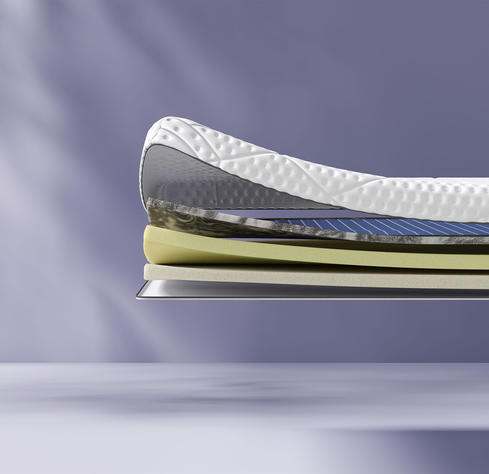 Coupe transversale d’un surmatelas montrant plusieurs couches, dont une couche supérieure texturée blanche et des couches intermédiaires bleues et jaunes. Le surmatelas porte l’inscription « Emma » sur le côté.