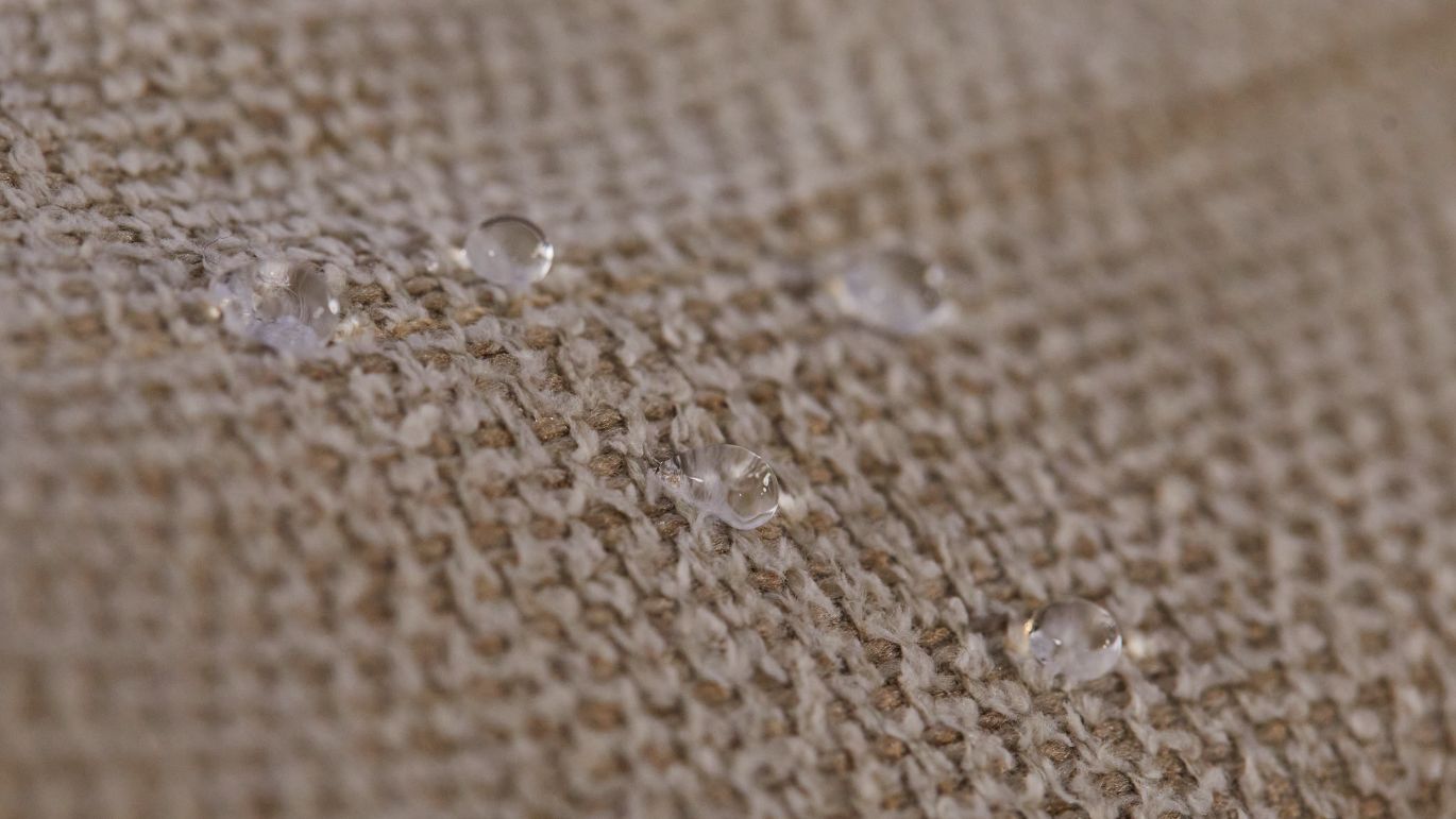 Gros plan sur un tissu tissé beige avec des gouttes d'eau à la surface, illustrant la déperlance