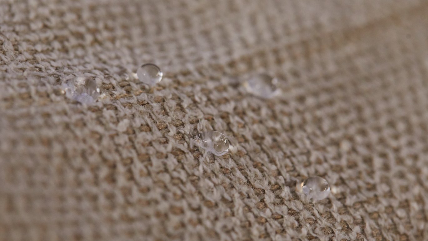 Gros plan sur un tissu tissé beige avec des gouttes d'eau à la surface, illustrant la déperlance