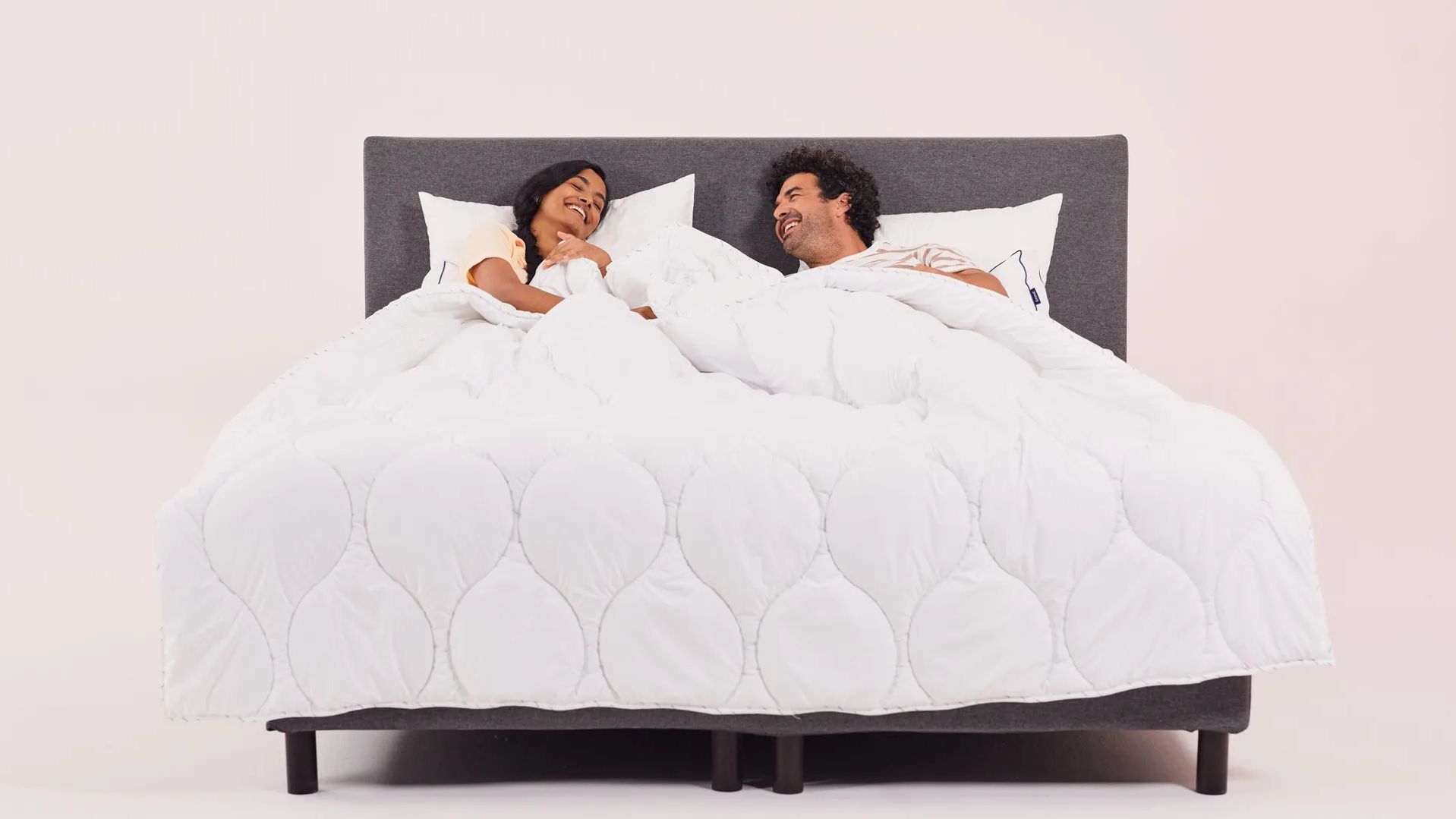 Imagem de um casal a rir, na sua cama, tapados por um edredon Emma Quente