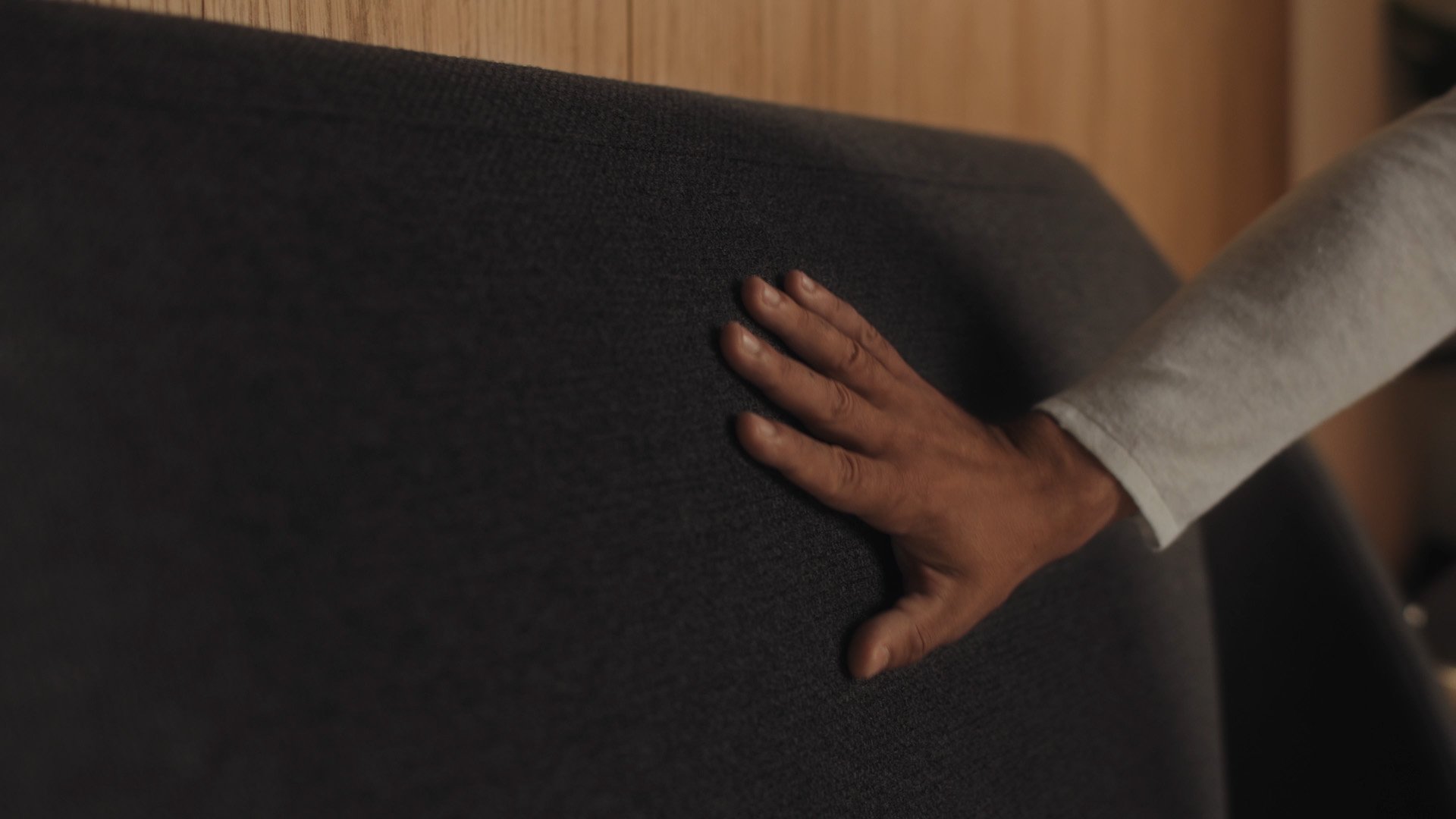 Close-up of hand touching the charcoal upholstered curved headboard of the Emma Performance boxspringbed.