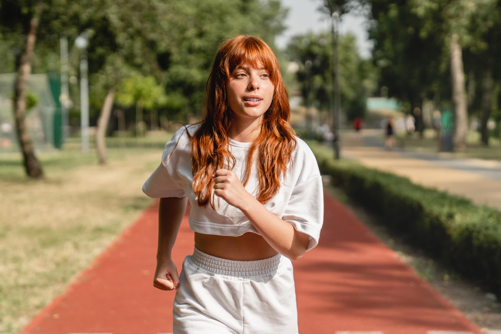 mujer joven pelirroja con chándal blanco está corriendo en un parque