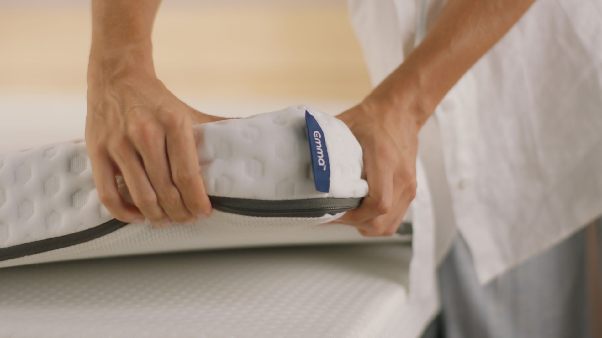 Persona che maneggia un topper arrotolato con rivestimento bianco testurizzato e etichetta blu 'Emma"