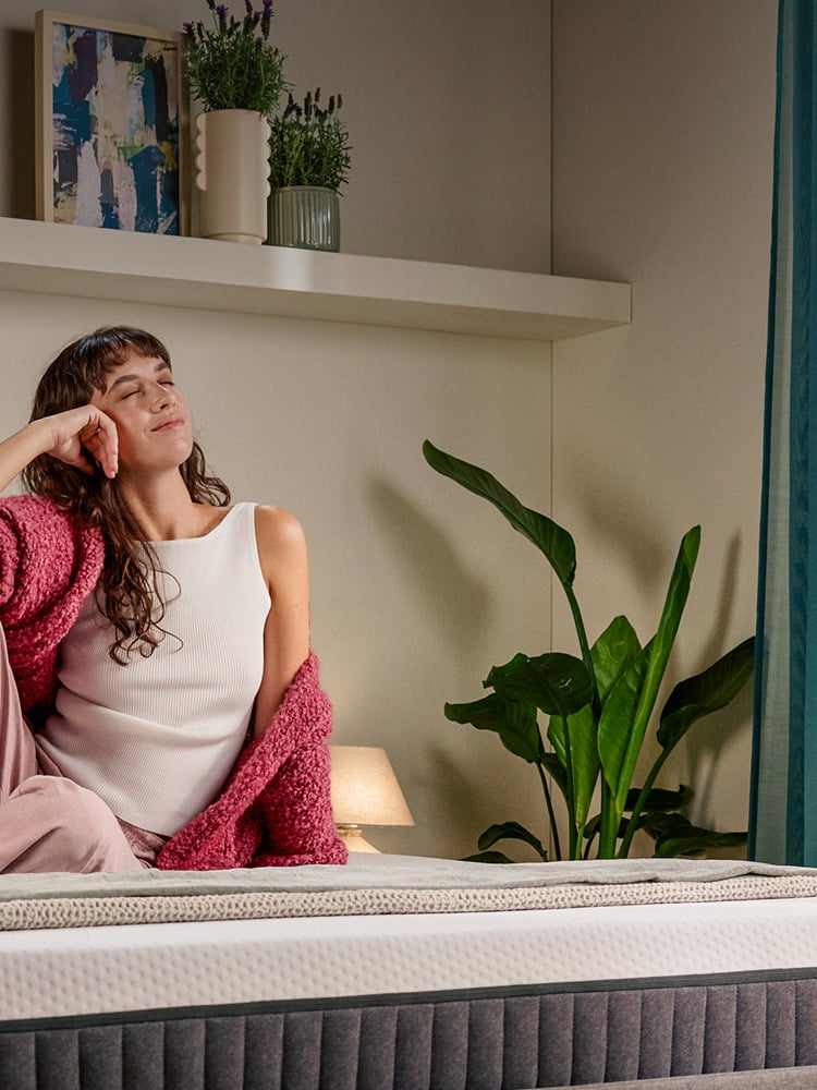 Mujer sentada en unca cama con colchón, en una habitación.