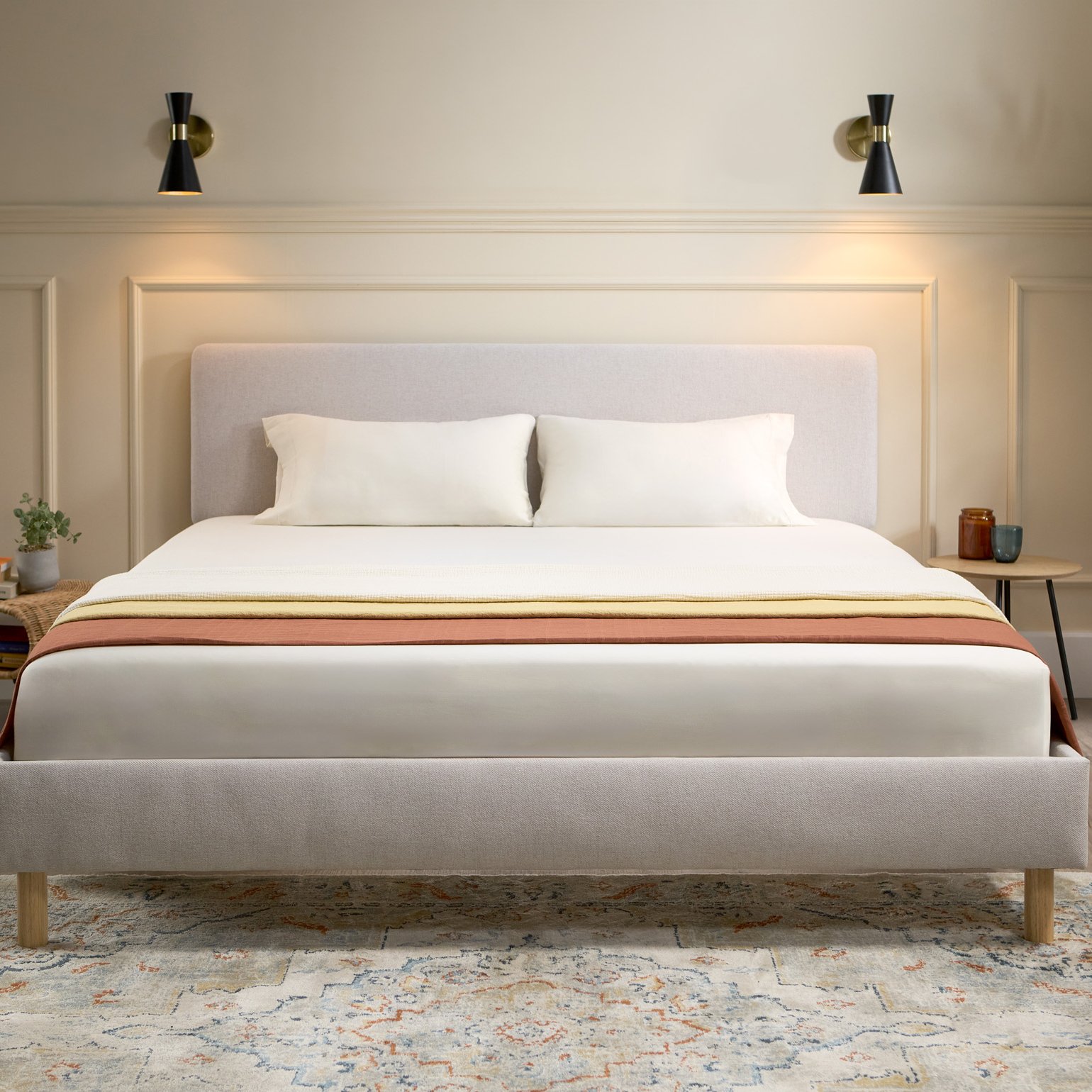 Emma Box Bed gris avec tête de lit rembourrée et pieds en bois, dans une chambre chaleureuse avec une grande fenêtre.