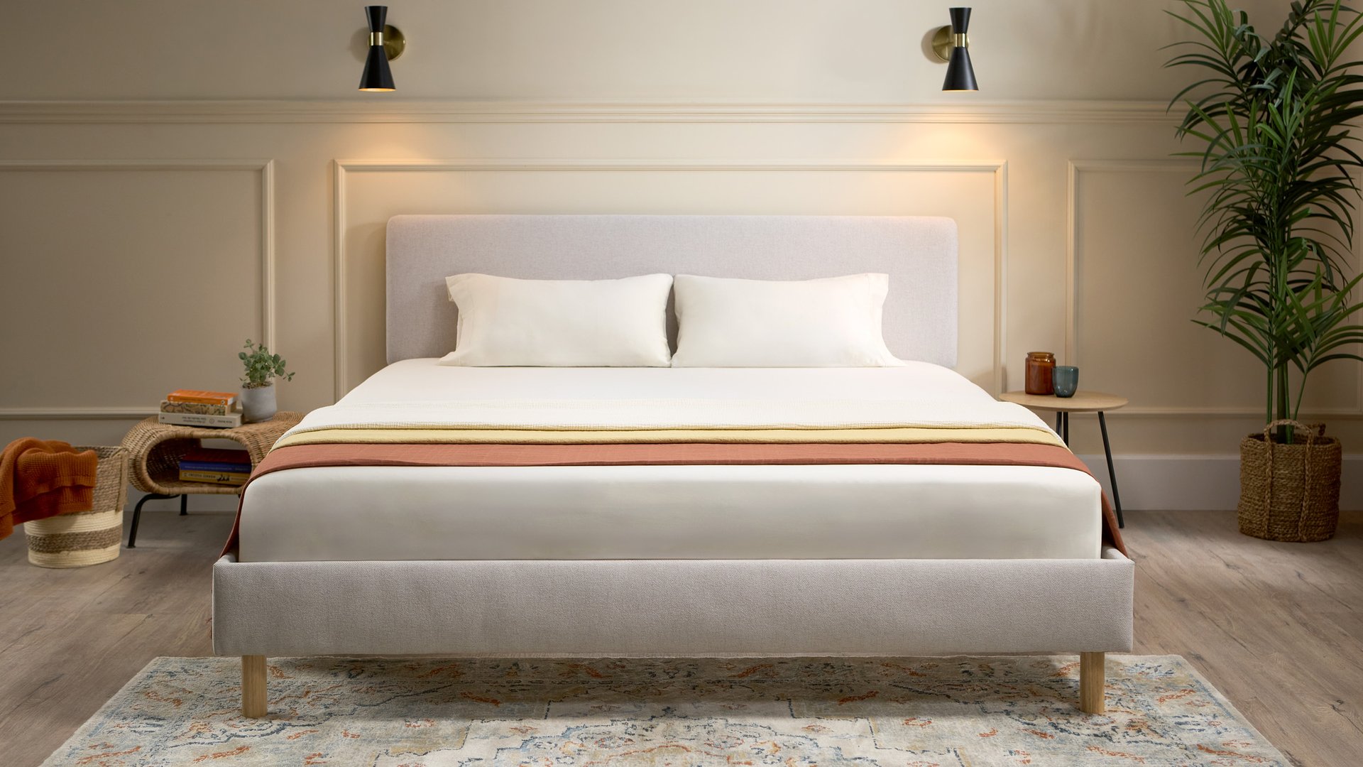 Emma Box Bed gris avec tête de lit rembourrée et pieds en bois, dans une chambre chaleureuse avec une grande fenêtre.