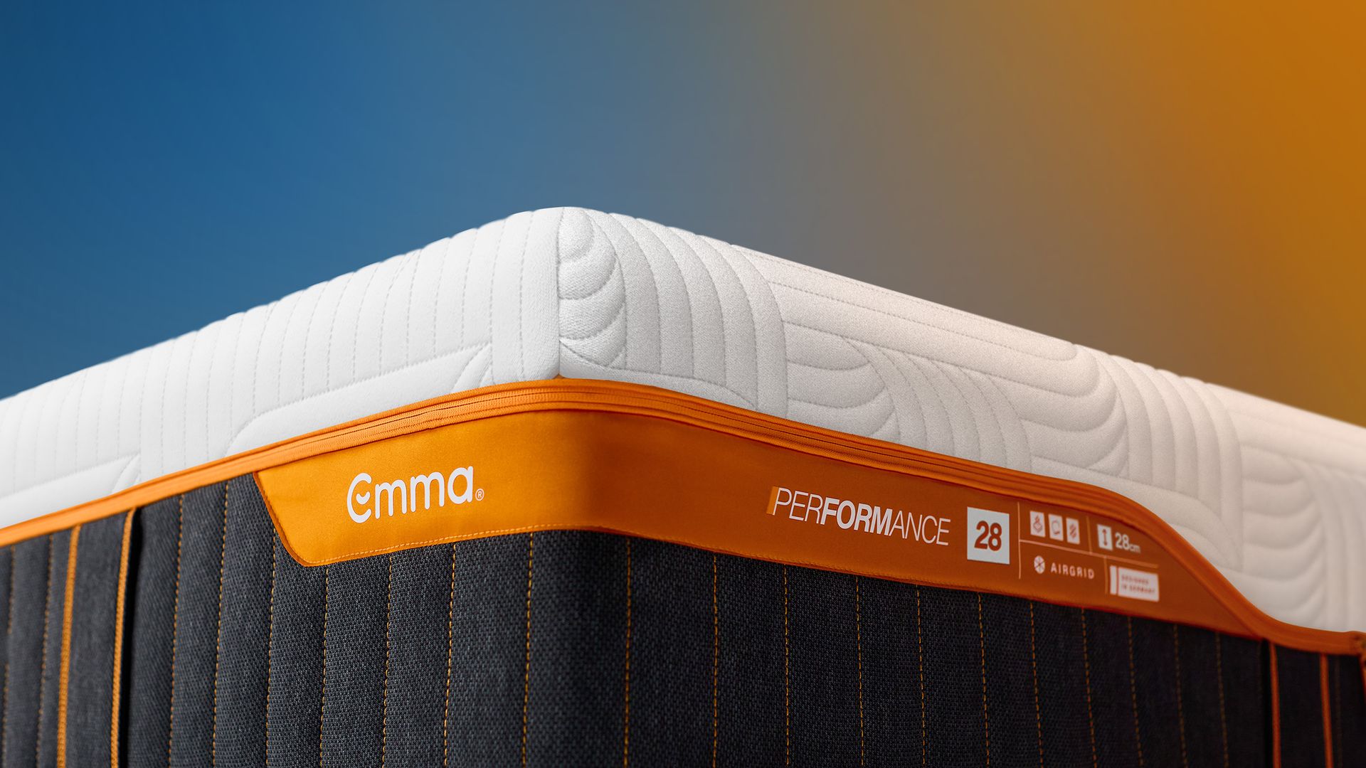 Close-up van een Emma-matras met witte bovenlaag en oranje rand met het label ‘Performance 28’.