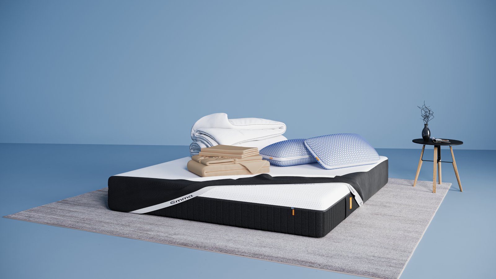 Ensemble de literie présenté dans une chambre moderne : matelas Hybride II ou Hybride Premium II avec base noire et surface blanche, partiellement recouvert d’un plaid gris foncé. Sur le matelas, deux oreillers Nuage Elite 40x70 cm bleus, une couette Nuage Tempérée blanche pliée, un protège-matelas, et une parure de lit en satin de coton blanc comprenant une housse de couette et des taies d’oreillers. Le tout est posé sur un tapis clair, avec une table d’appoint noire à pieds en bois et une décoration minimaliste.