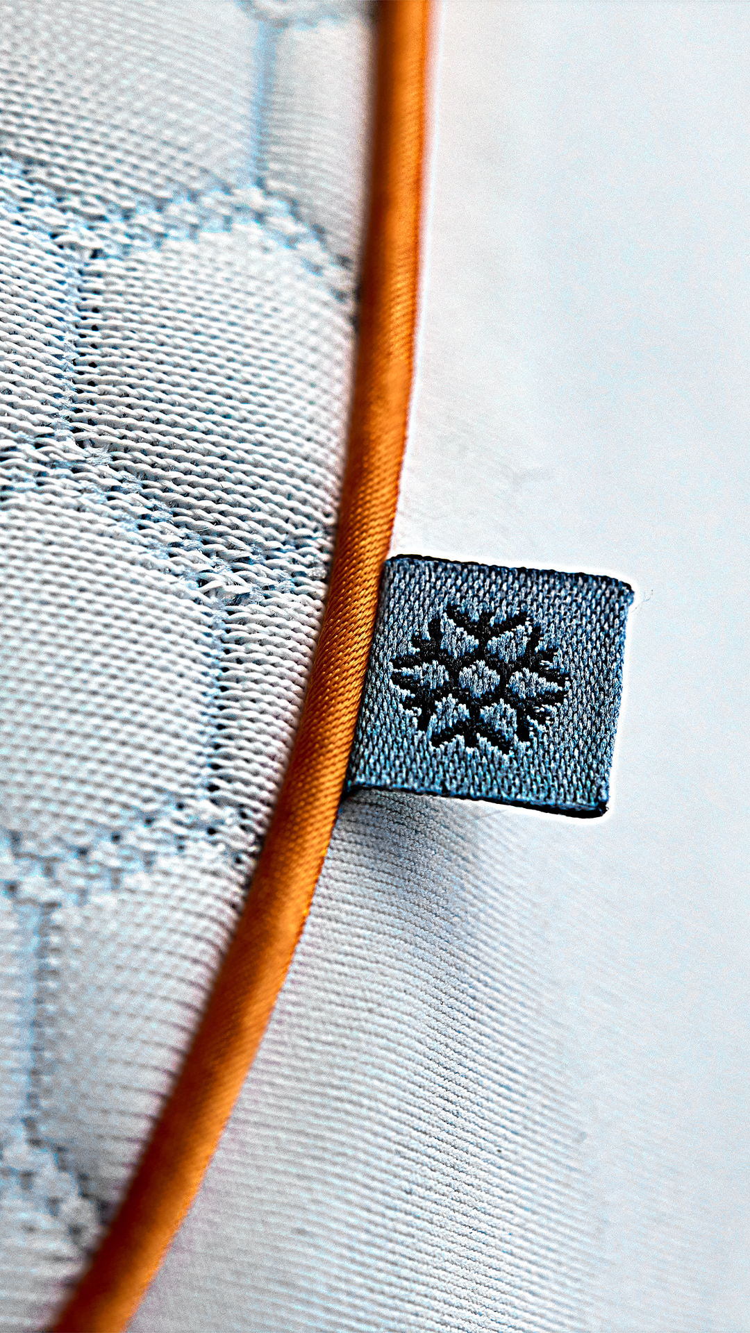 Close-up of Emma Performance Hybrid Pillow corner showing hexagonal-stitched cover, orange trim, and cooling label.