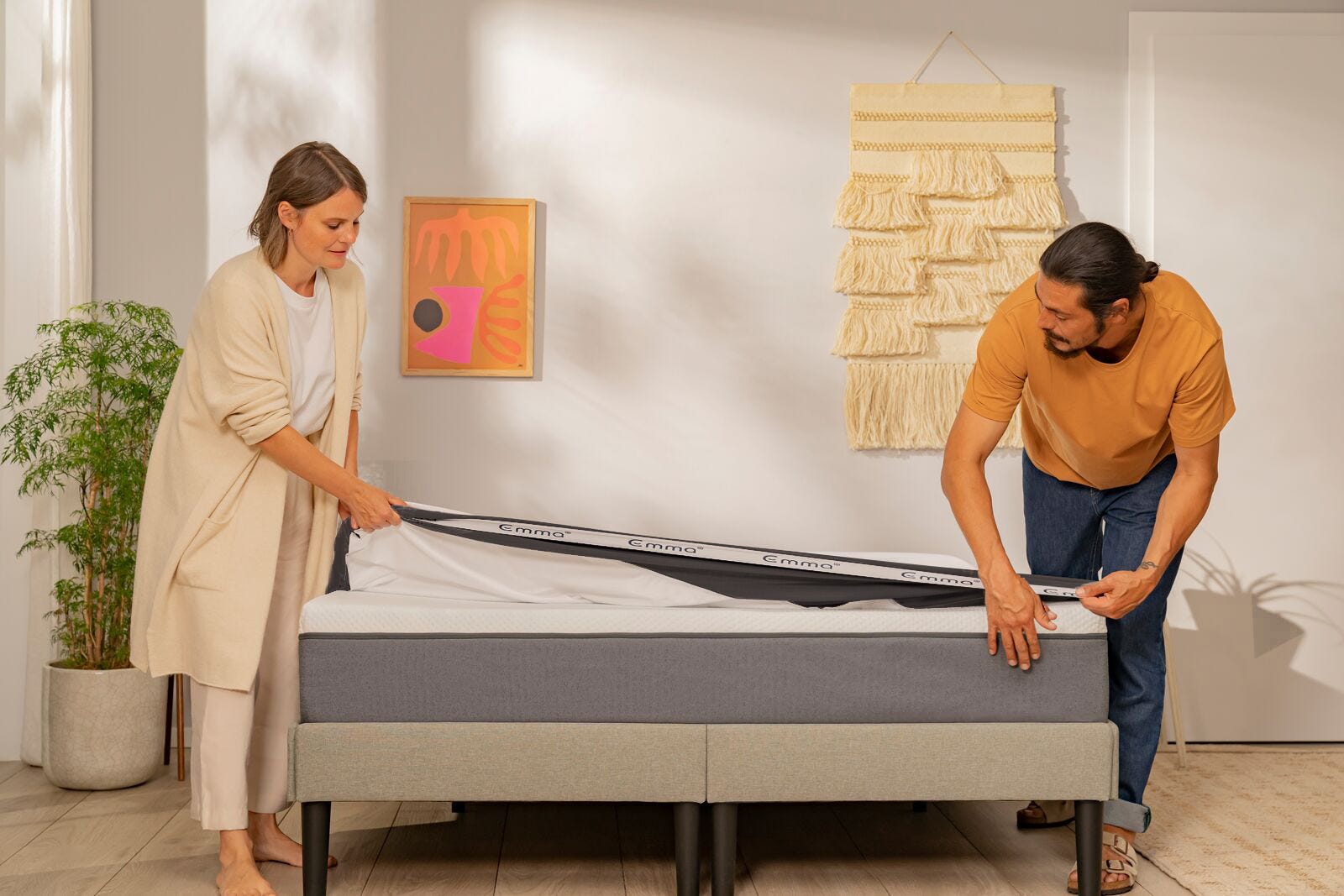 A man and a woman smiling while tucking a mattress protector on top of a mattress.