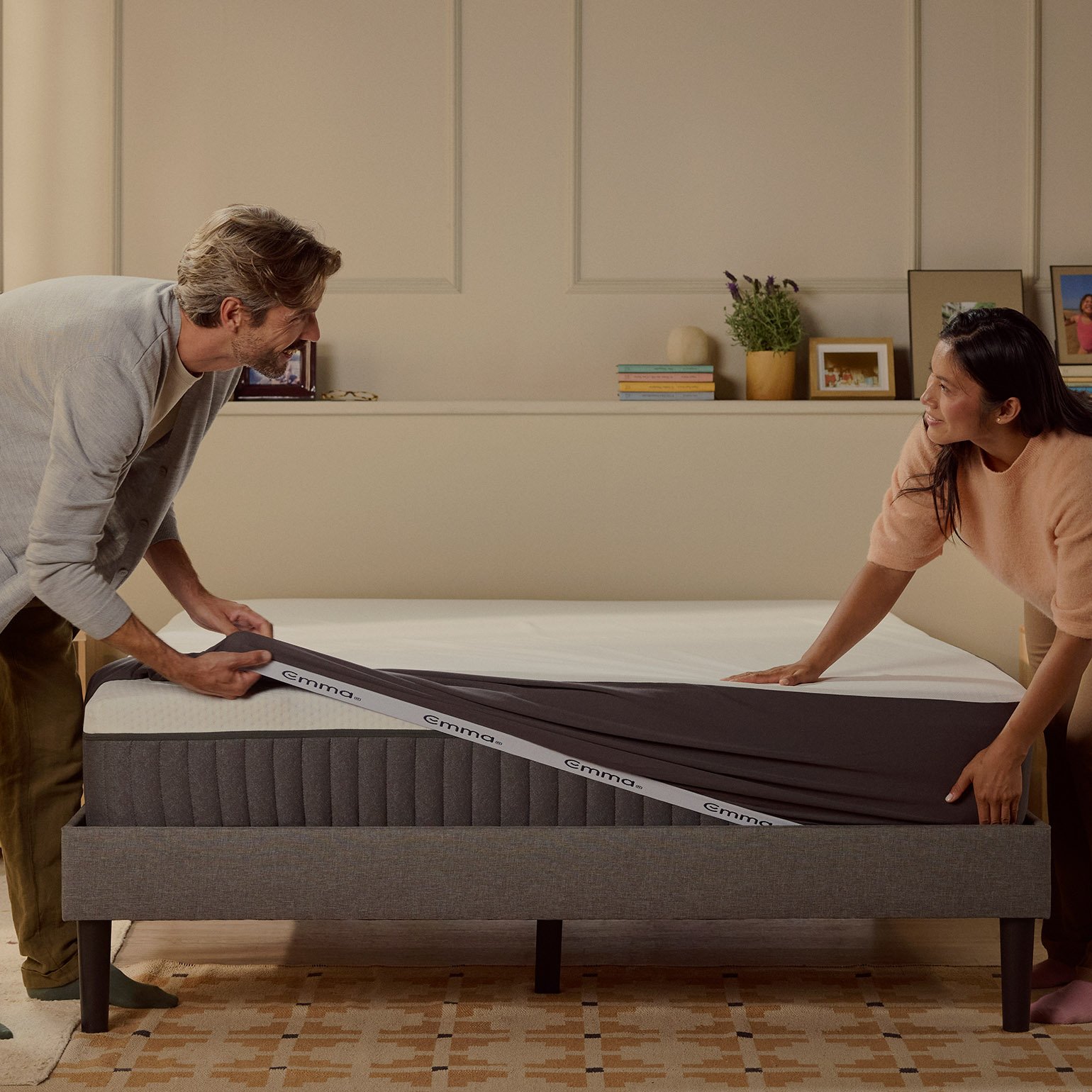 Paar zieht Emma Premium Matratzenschoner über eine Matratze im Schlafzimmer.