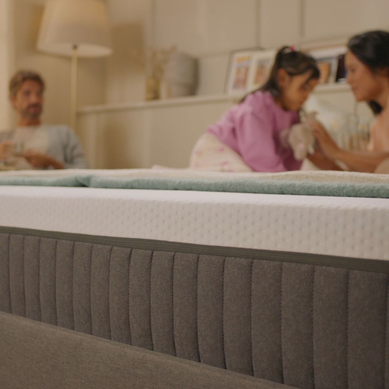 Close-up of the Emma Original mattress with a family relaxing together in the background.