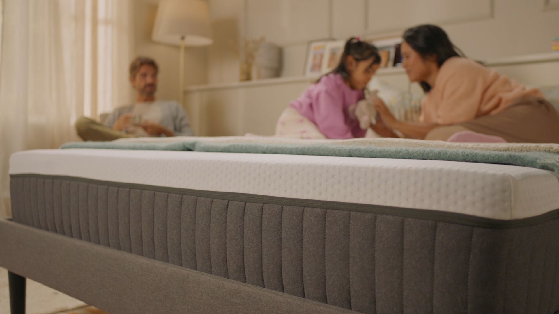 Close-up of the Emma Original mattress with a family relaxing together in the background.