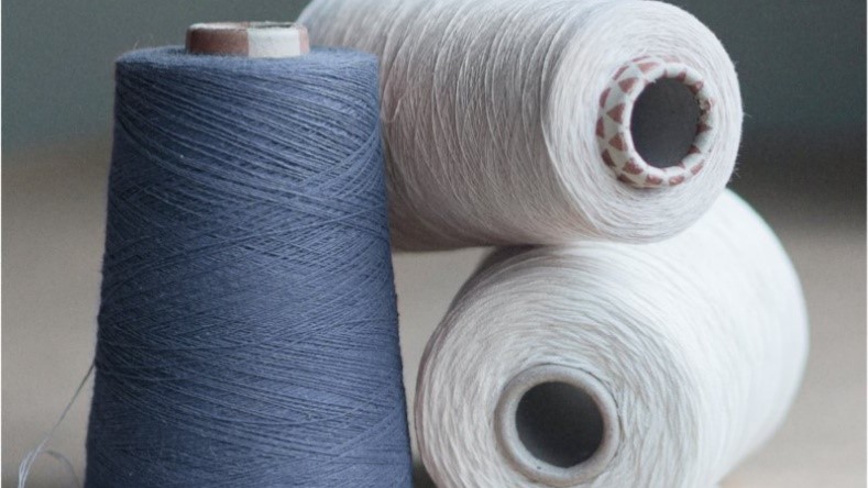 Drei Garnrollen in Blau und Weiß auf einem Tisch liegend.