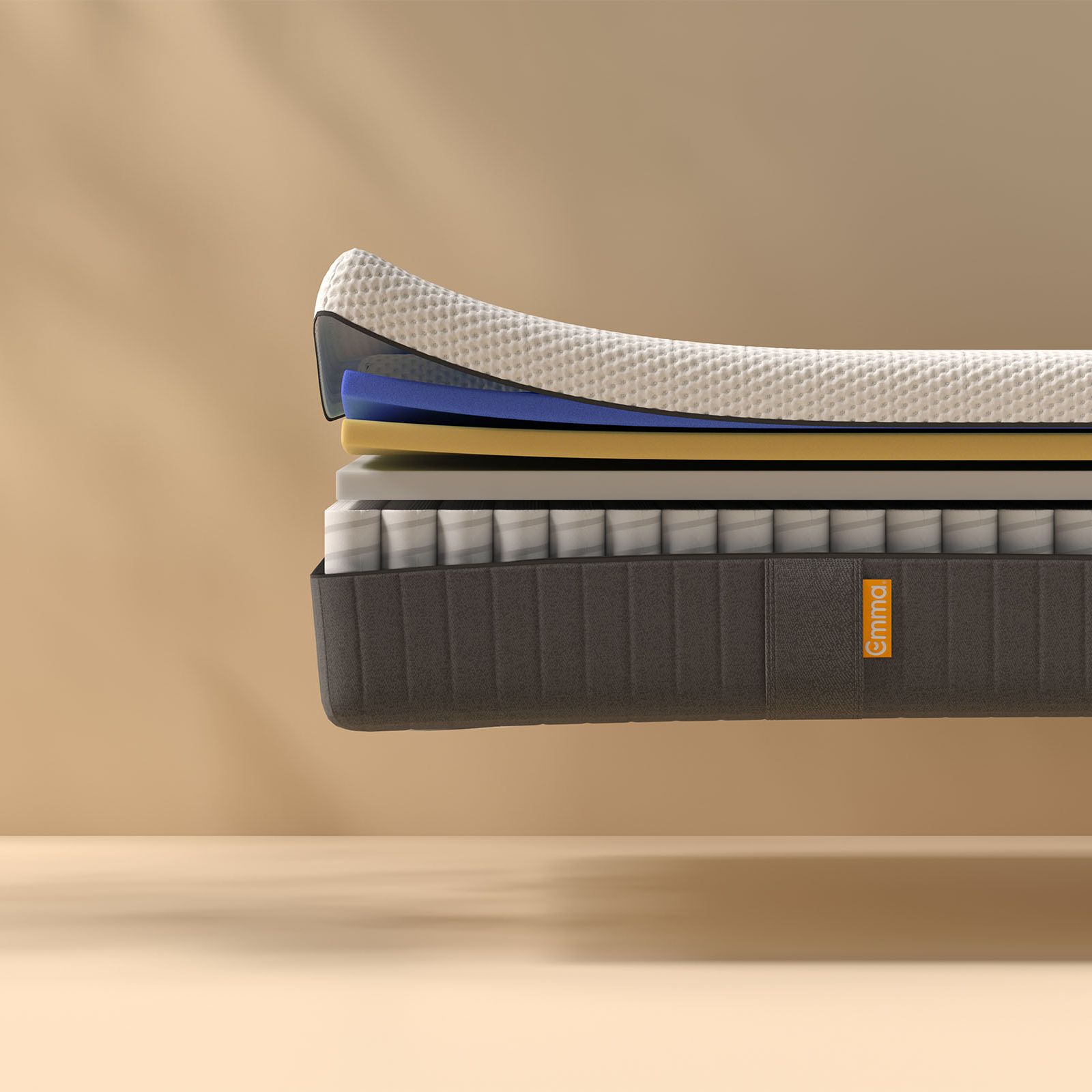Coupe transversale d'un matelas montrant plusieurs couches, dont une couche supérieure texturée blanche, des couches intermédiaires bleues et jaunes, et un sommier dont les ressorts sont visibles. Le matelas porte l'inscription "Emma" sur le côté.
