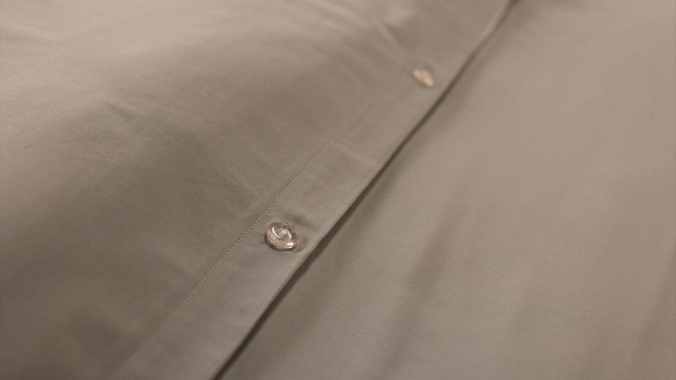 Close-up of button closure on a grey-green duvet cover.