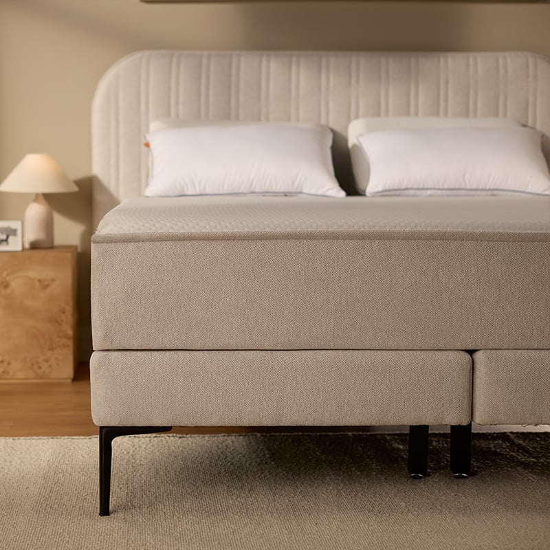 Beige upholstered bed with white mattress and pillows.