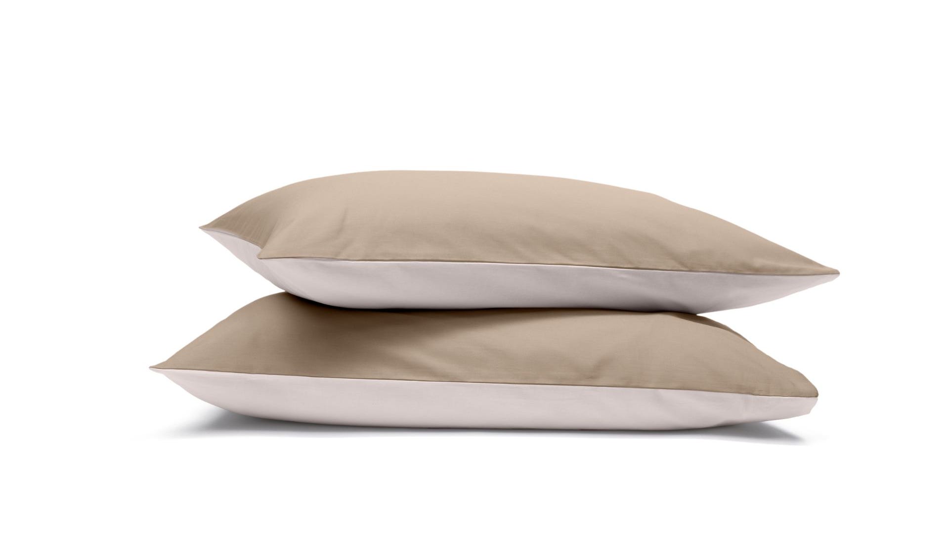 Due federe beige e bianche impilate su sfondo bianco.