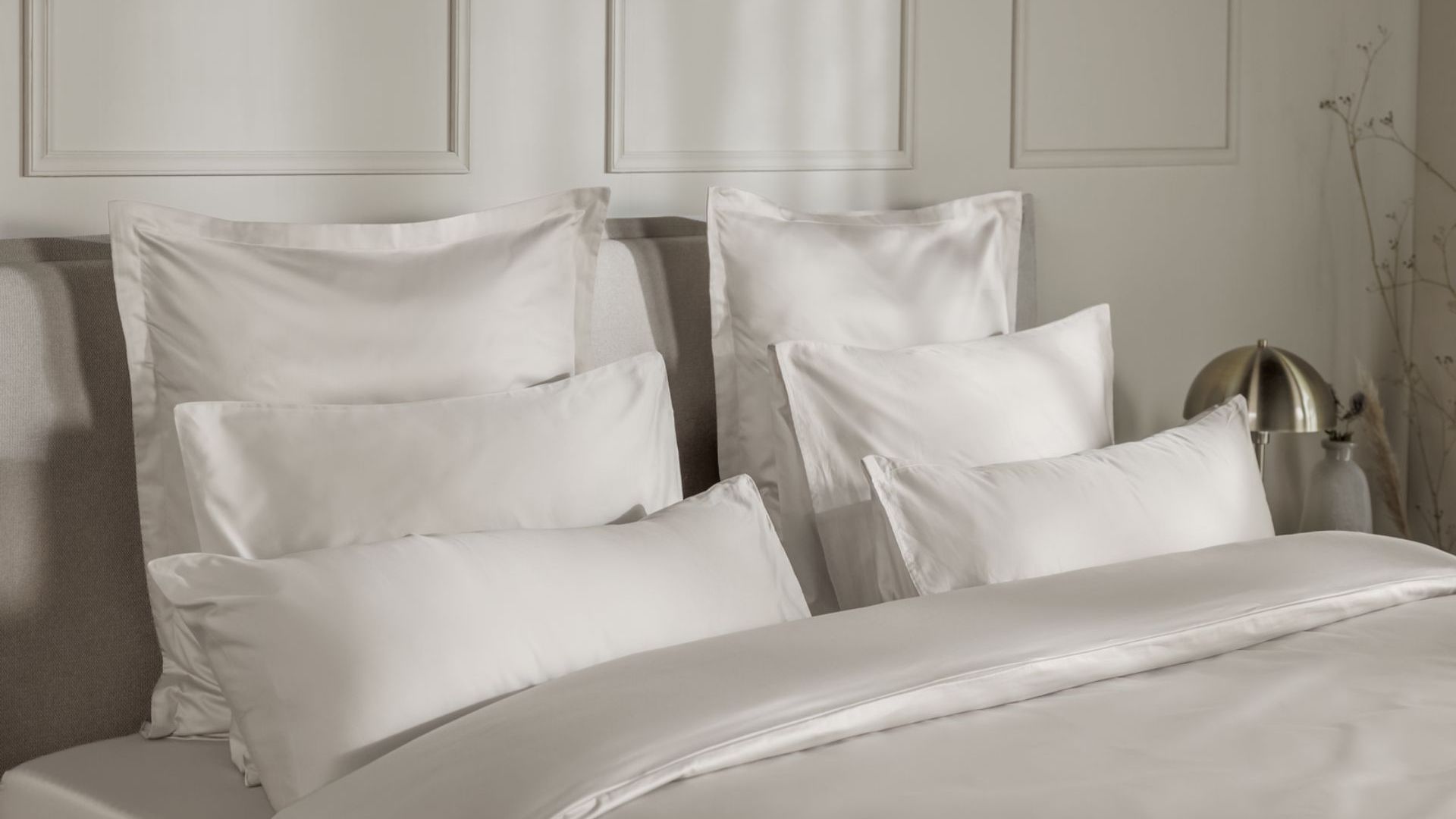 Letto con federe e copripiumino beige, contro una parete con pannelli decorativi.