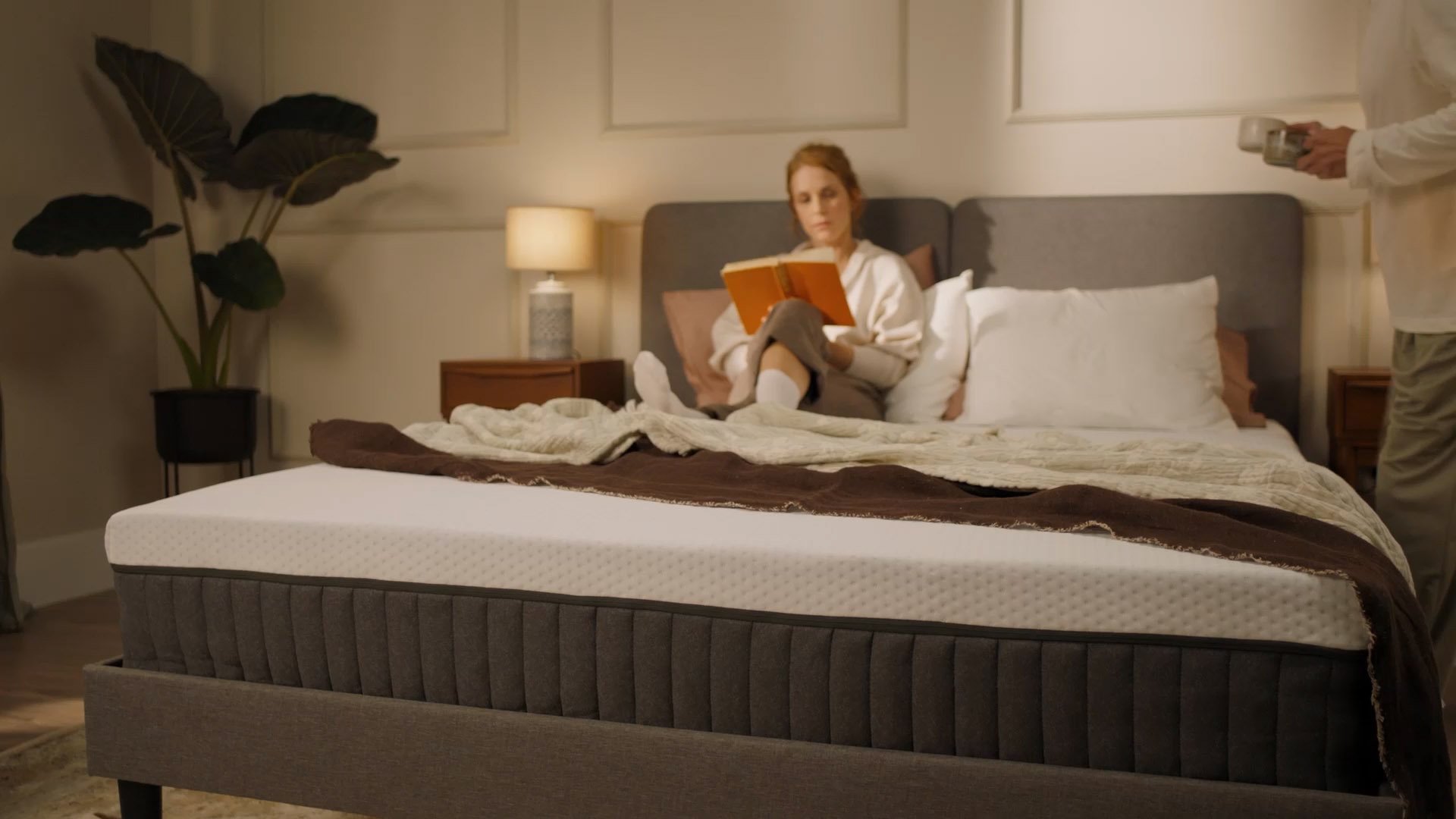 Person sitting on a bed with a white mattress in a bright bedroom.