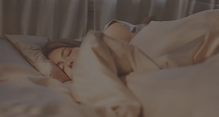 A person sleeping comfortably in soft beige bedding, with an Emma mattress and an orange heart graphic displayed beside them.