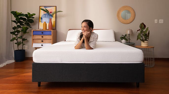 Vrouw leunt ontspannen op een Emma-matras in een stijlvol ingerichte slaapkamer met moderne en natuurlijke accenten.