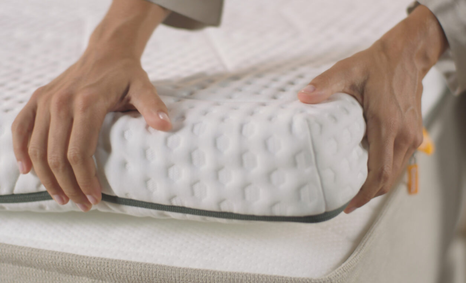 Des mains posant un surmatelas blanc sur un lit au design capitonné avec une bordure noire.