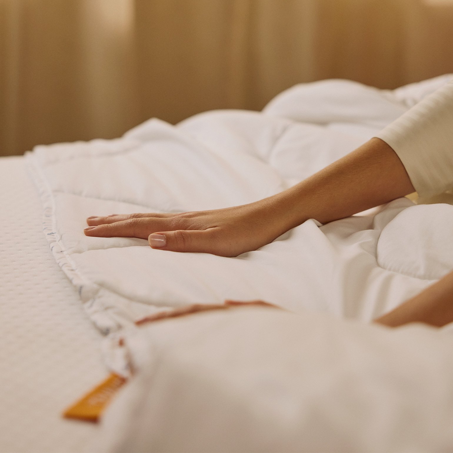Hands feeling a stretched duvet on top of a mattress.