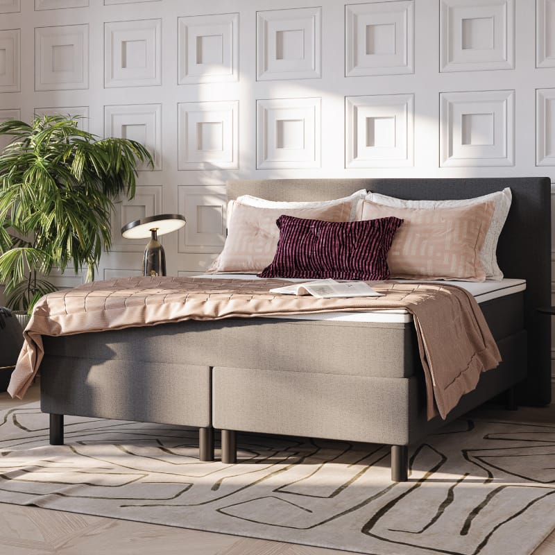 Boxspringbett mit beiger Tagesdecke und Zierkissen in stilvollem Schlafzimmer